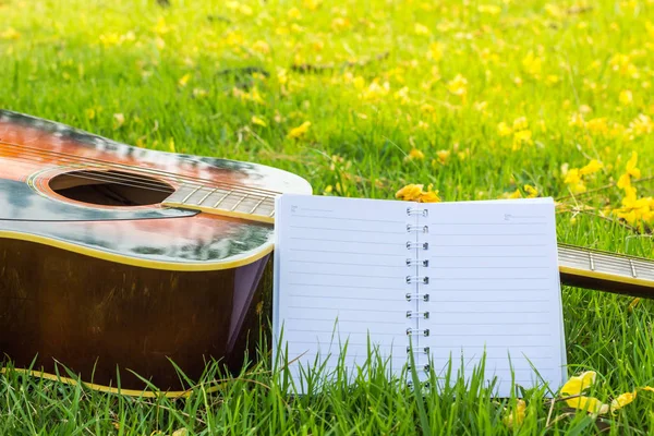 Paper for writing songs with a guitar on the lawn background.