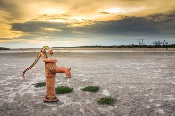Rusty water pump on barren ground sunset