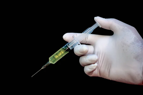 Sprutan i en hand i medicinska handskar, redo för injektion med medicinering. svart bakgrund — Stockfoto