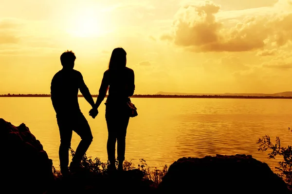 Siluetter av man och kvinna som håller händerna medan vid solnedgången — Stockfoto