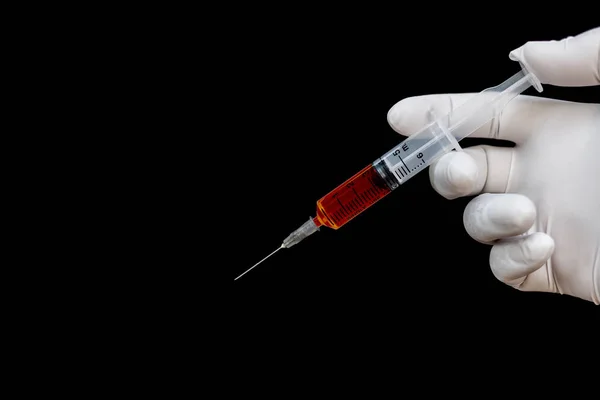 Sprutan i en hand i medicinska handskar, redo för injektion med medicinering. svart bakgrund — Stockfoto