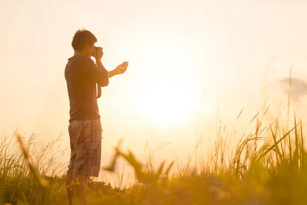 O jovem está a olhar para o pôr-do-sol. Viajante com câmera — Fotografia de Stock