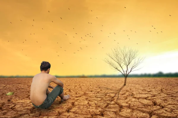 O homem senta-se na terra rachada perto da terra seca e ar seco quente . — Fotografia de Stock