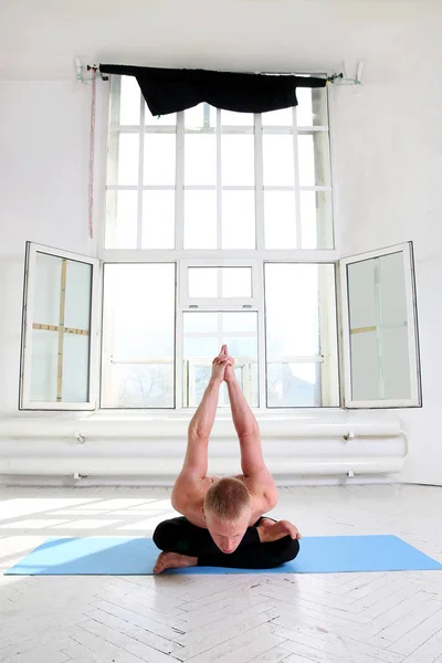 Sportovní muž cvičení jógy v bílé místnosti s velkým oknem — Stock fotografie