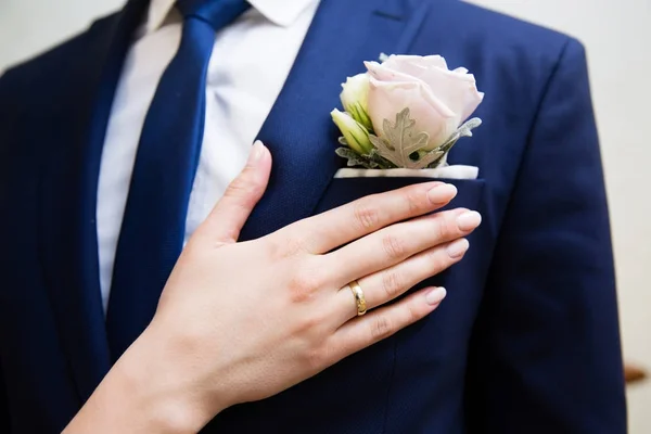 Wedding boutonniere on suit of groom and brides hand — Stock Photo, Image