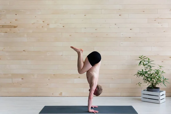 Sporty man practices yoga handstand asana Adho Mukha Vrikshasana at the yoga studio. Balance exercise