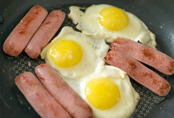 Fried eggs with sausages, 3 fried eggs, several sausages on a bl — Stock Photo, Image