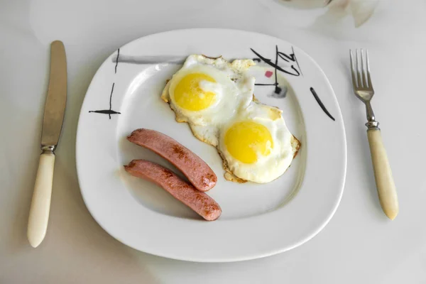 Gebakken eieren met worst op een bord, mes en vork — Stockfoto