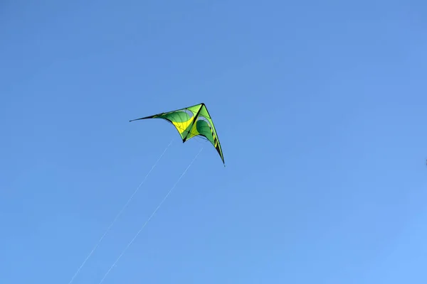 Треугольный желтый с зеленым змеем, плавающим в голубом небе — стоковое фото