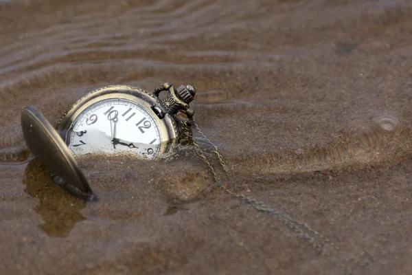 水の下の濡れた砂の上に横たわる手で丸い時計 — ストック写真