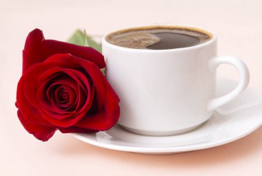 Bir fincan sade kahve, çay tabağı, kırmızı gül çiçeği., 