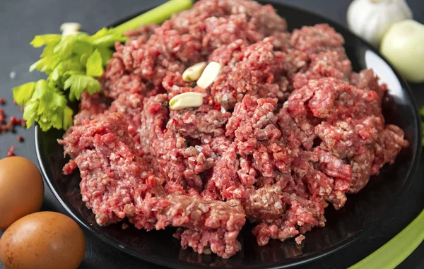 Carne picada crua fresca com dentes de alho em uma placa preta — Fotografia de Stock