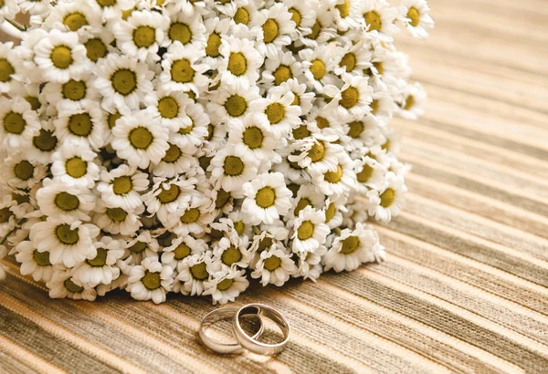 wedding bouquet of field daisies, 2 gold wedding rings on beige