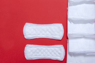 Kadın günlük hijyenik pedleri, kırmızı arka planda birkaç ince ped.