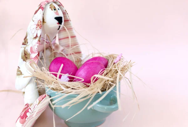 Рожеві Великодні яйця з сіном і пасхальними зайцями на бежевому тлі., — стокове фото