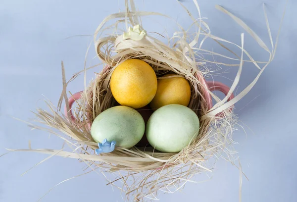 Amarillo, huevos de Pascua verdes en el heno en un plato de color rosa en un b azul — Foto de Stock