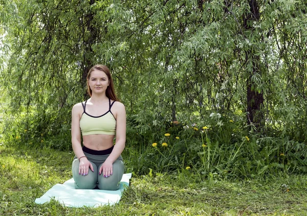 1 młoda kobieta w odzieży sportowej siedzi na zielonej Mata jogi wśród th — Zdjęcie stockowe