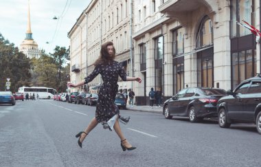woman in a long dress runs across the street in the city against