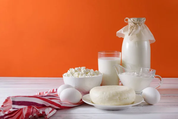glass of milk, a bottle of milk, eggs, cottage cheese, cheese, sour cream, a towel on an orange background,