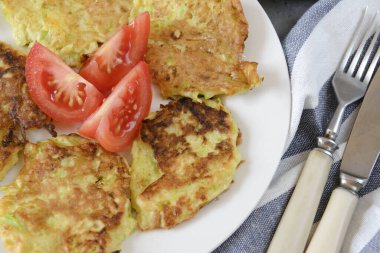 Yakın plan bir tabakta domates dilimli kabak krepleri, çatal, bıçak, sebze krepleri.