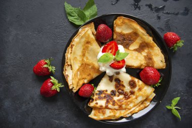 3 krep ve çilek ve krem şanti siyah arka planda bir tabakta, üst manzara,