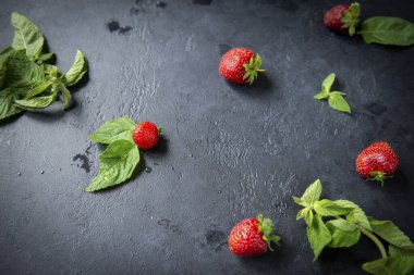 Siyah arka planda yeşil naneli, olgun kırmızı çilekler.