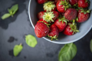 Koyu arkaplan manzaralı bir tabakta olgun kırmızı çilekler, nane yaprakları.
