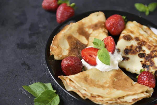 stock image pancakes with whipped cream and mint on a plate on a black background