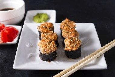 Balık ve susamlı Japon çörekleri. Norveç yosunu, zencefil ve wasabi 'de. Siyah arka planda beyaz bir tabağa yapışıyor.