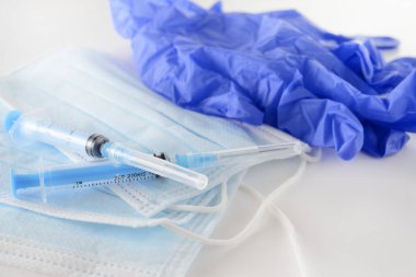 İlaç şırıngası, mavi tıbbi maskeler, beyaz arka planda tıbbi eldivenler, ilaçlar.