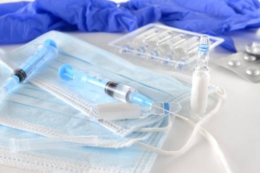 İlaçlı şırıngalar, mavi tıbbi maskeler, tıbbi eldivenler, beyaz arka planda aşı şişeleri, ilaçlar.