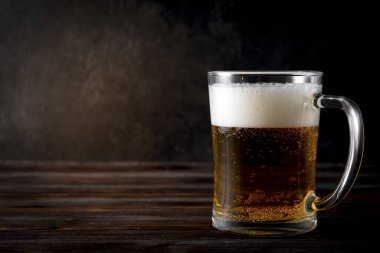 Koyu ahşap arka planda köpüklü 1 kupa light bira, alkollü içecek.