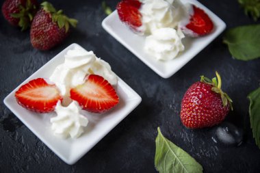 Tatlı, krem şantili çilek, siyah arkaplanda nane yaprakları, taze böğürtlen, yakın plan.