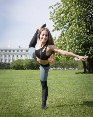 Bir yaz günü taytlı bir beyaz kız parkta yoga yapıyor.