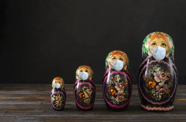 several Russian dolls in a medical mask on a black background, protection from coronavirus