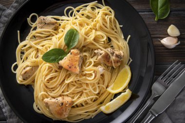 makarna, spagetti tavuk filetosu, limon dilimleri, sarımsak, yeşillikler, ıspanak, peçete, çatal, bıçak siyah tabakta, kapan, üst manzara