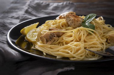  Siyah tabakta tavuk filetosu, peçete, siyah ahşap arka planda makarna.