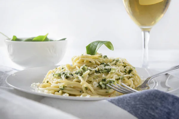 1 plate of pasta with spinach and cheese, a glass of wine on a white wooden background close up