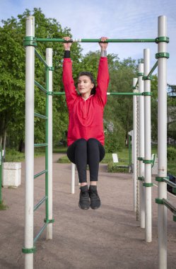 Spor, taytlı bir beyaz kadın ve spor sahasında yatay bir barda asılı kırmızı bir ceket., 