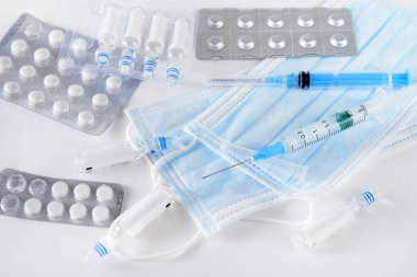 İlaçlar, ampuller, mavi tıbbi maskeler, beyaz arka planda şırıngalar, üst manzara