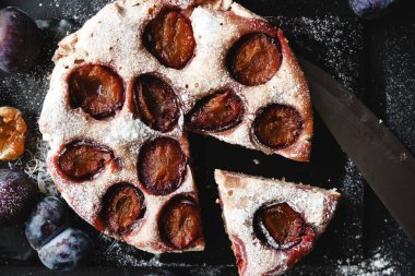 Koyu bir masada taze erikli erik turtası, 2 bardak erik likörü, bir parça tatlı böğürtlenli turta
