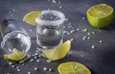 İki bardak gümüş tekila, tuz ve gri arka planda dilimler, güçlü bir alkollü içecek.