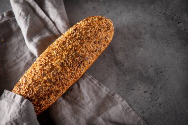 Gri arka planda gri bir havlunun üzerinde bir somun taze tahıllı ekmek, yiyecek, üst manzara