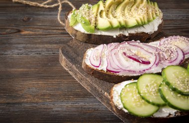3 sandviçli peynir, avokado, soğan, salatalık ve susam. Koyu ahşap zemin üzerinde. Kahvaltı, atıştırmalık, fotokopi alanı.,