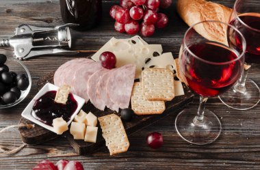 Kırmızı şaraplı aperatif, peynirli kraker, jambon, zeytin, reçel, üzüm, baget, tirbuşon, koyu ahşap arka plan, üst görünüm, 