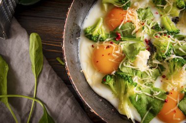 Peynirli sahanda yumurta, brokoli, siyah ahşap arka planda ıspanak, protein sağlıklı kahvaltı.