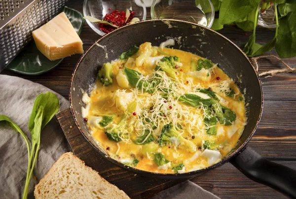 protein healthy Breakfast , fried eggs with  broccoli,  spinach, cheese in a pan on a dark wooden background, top view