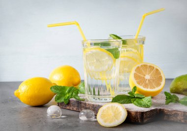 2 bardak limonata, sarı limon ve nane, gri ve mavi arka planda buz, taze narenciye, ferahlatıcı içecek.