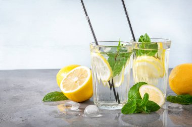 2 bardak limonata, sarı limon ve nane, buz, gri ve mavi arka planda kokteyl tüpleri, taze narenciye, ferahlatıcı içecek.