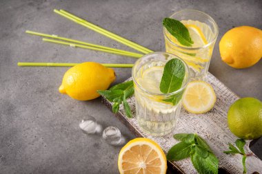 Sarı limonlu 2 bardak limonata ve gri arka planda nane şekeri, taze narenciye, ferahlatıcı içecek.